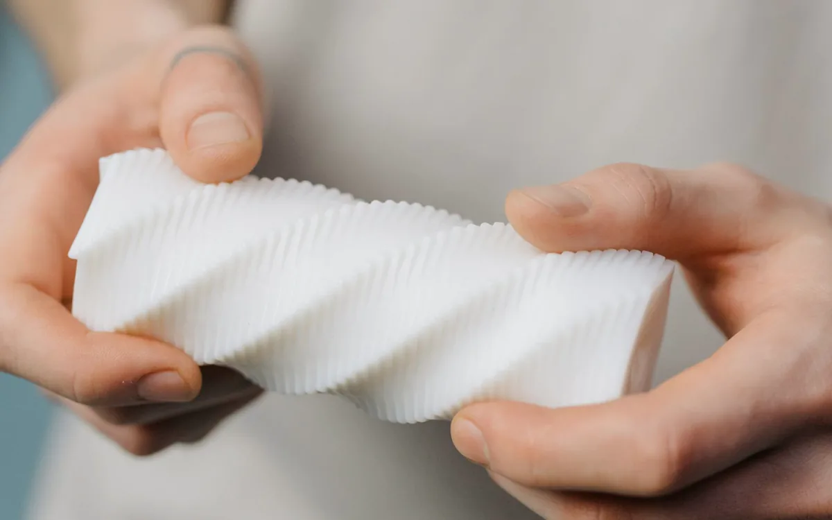 Hände halten ein weißes, spiralförmig 3D-gedrucktes Objekt