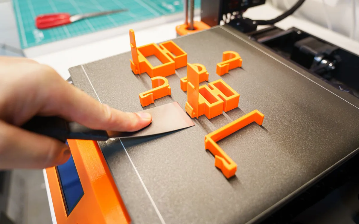 Mehrere orangefarbene 3D-gedruckte Teile werden von der Druckplatte gelöst