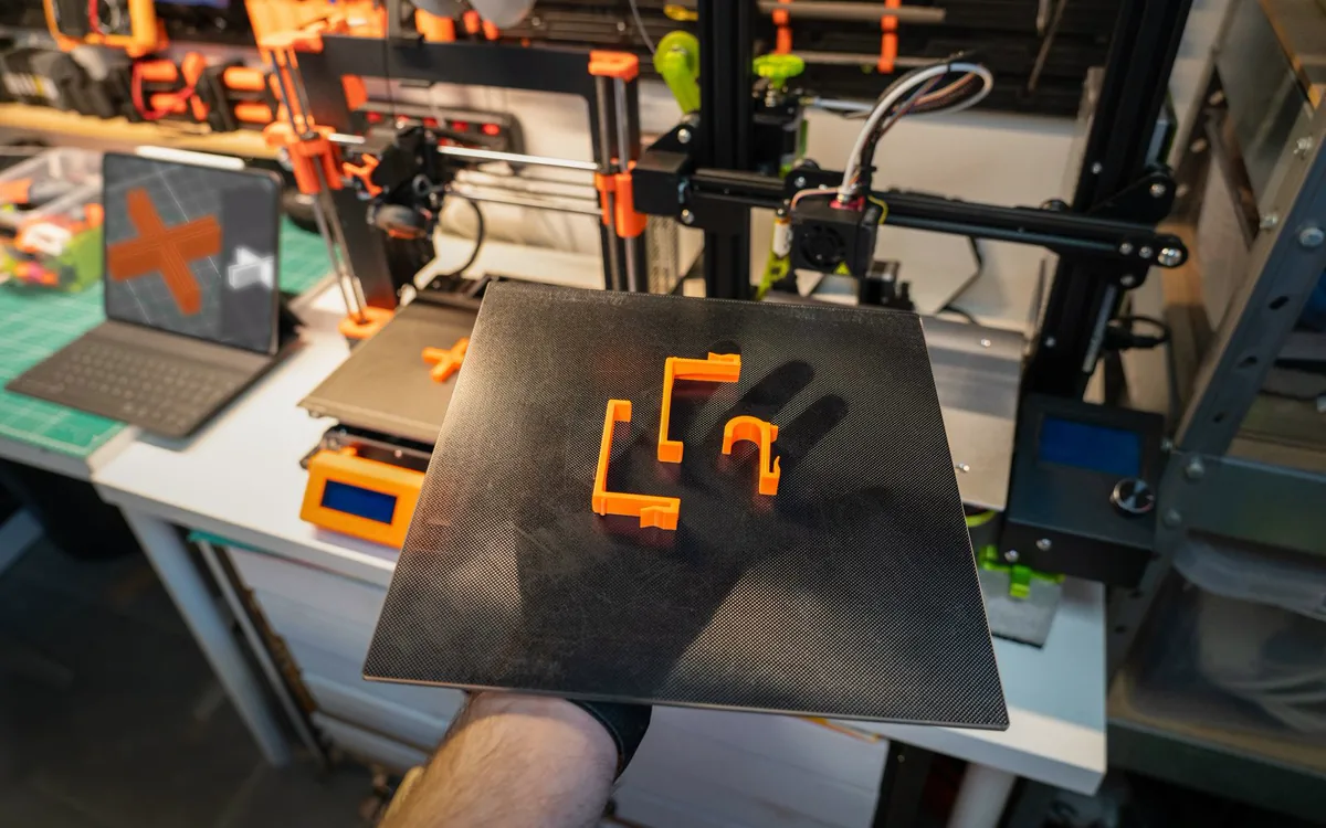 3D-Drucker mit einem frisch gedruckten orangefarbenen Bauteil auf der Druckplatte
